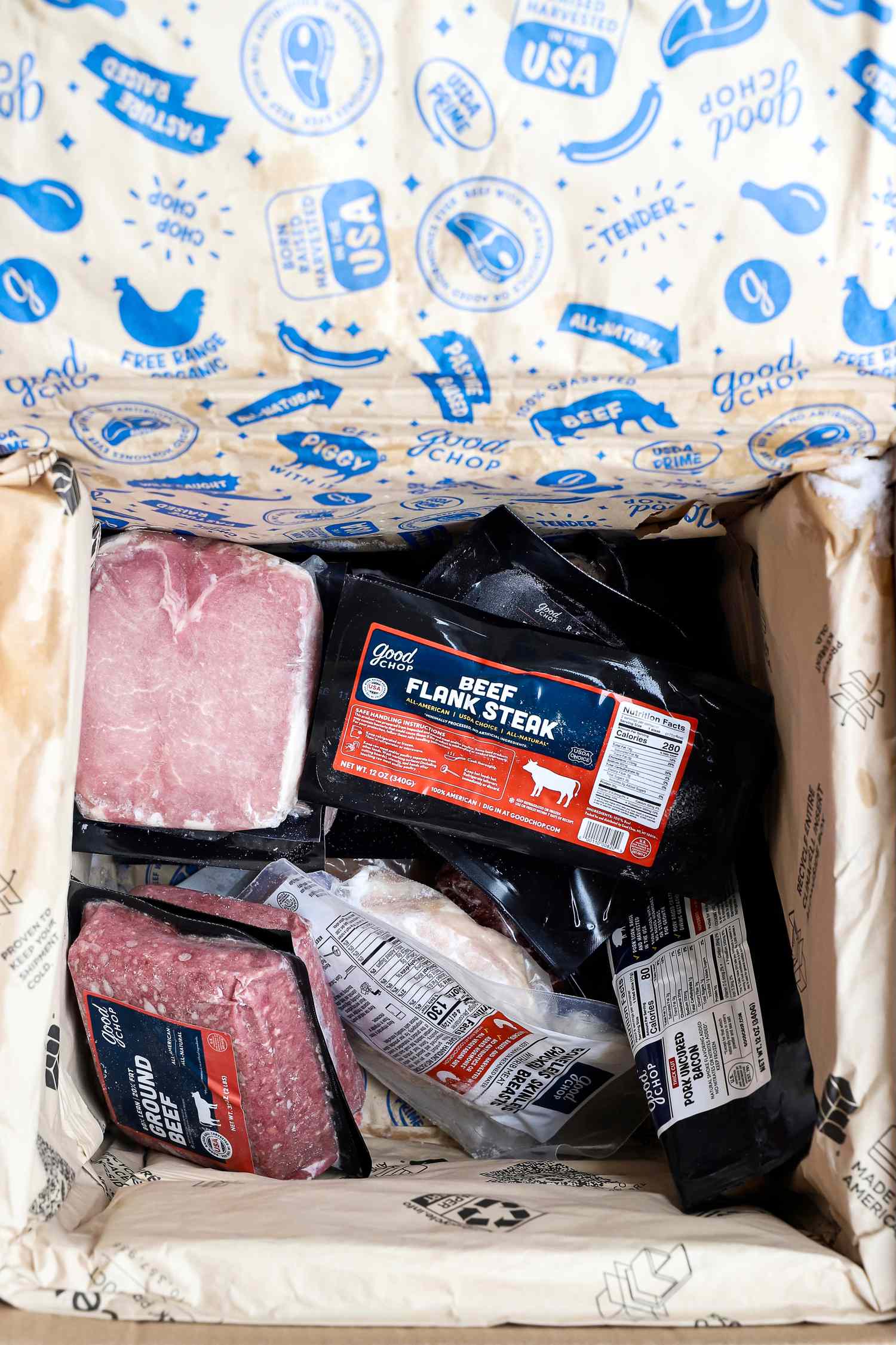 An opened Good Chop box containing various vacuumsealed packages of meat products with visible labels