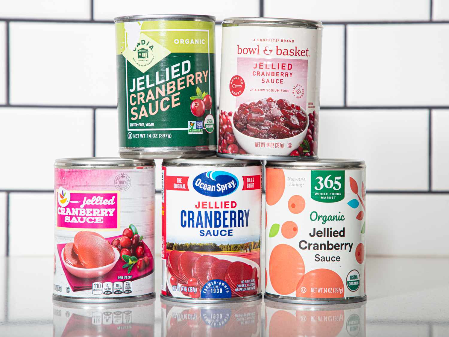 Five different cans of jellied cranberry sauce stacked together on a kitchen countertop