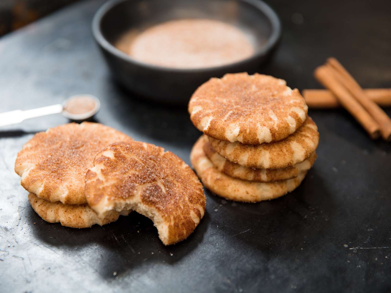 Close up view of a stack of snickerdoodle cookies with a bowl of cinnamon sugar in the background.