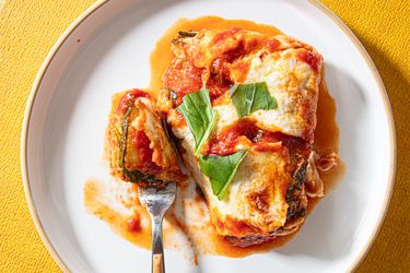 A plate with a zucchini parmesan dish garnished with basil accompanied by a fork