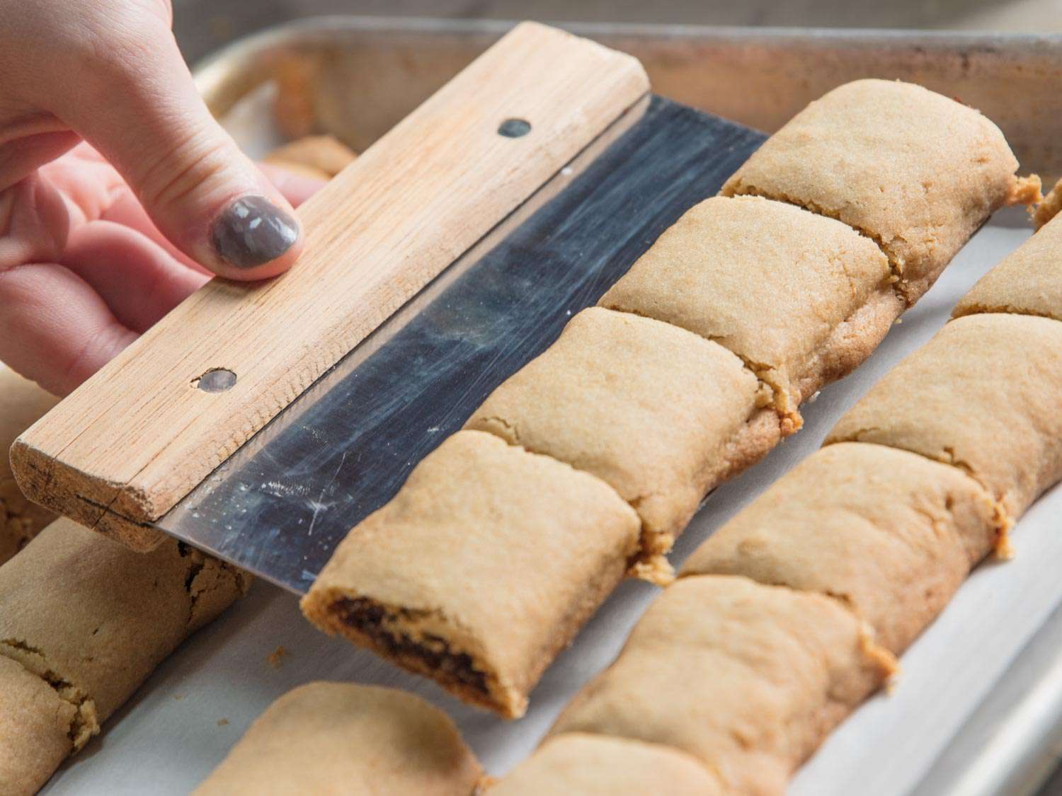 Golden-hued BraveTart's Fig Newtons being lifted off baking sheet with a dough scraper.