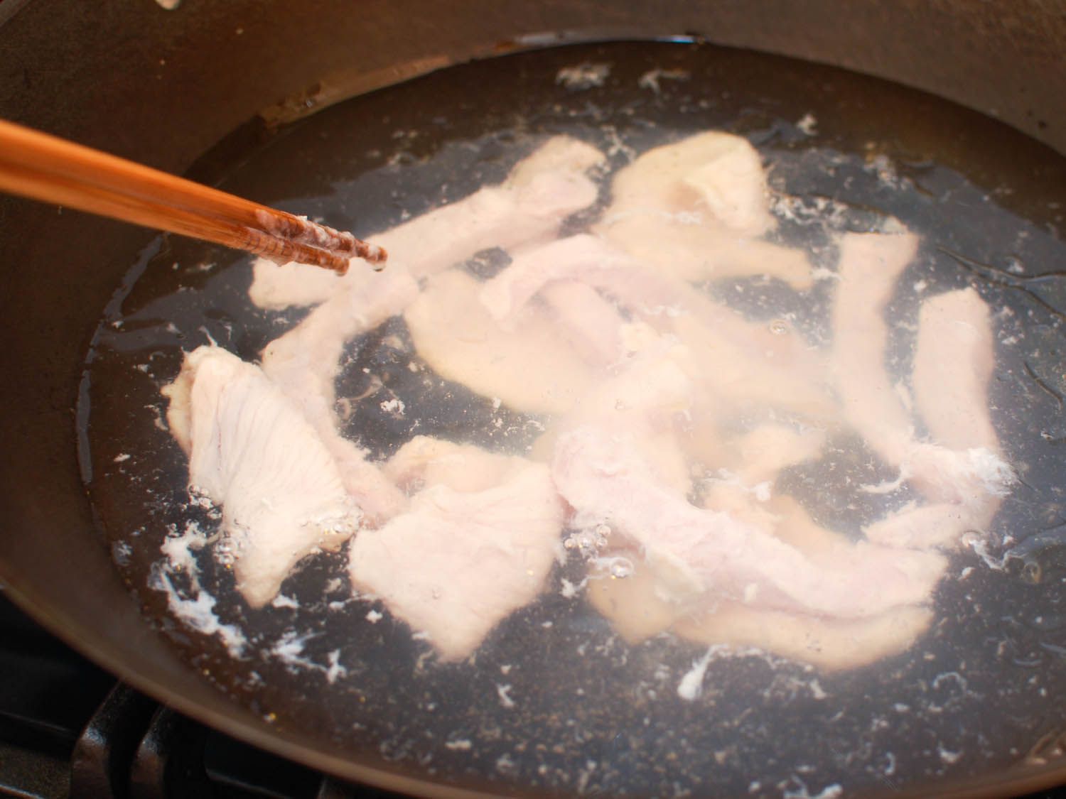 Meats being water-velveted in a wok.