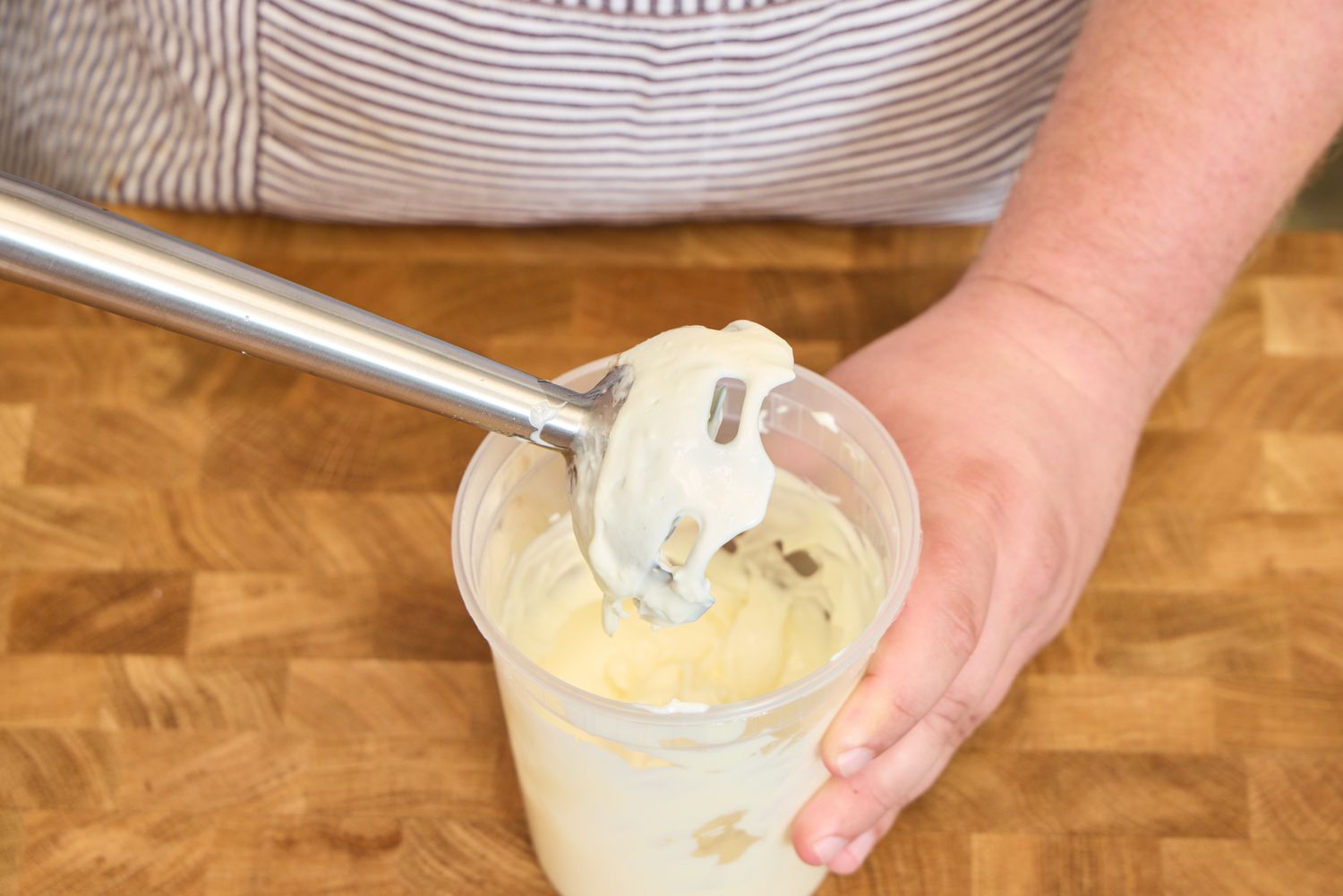A person uses the All-Clad Stainless Steel Immersion Blender inside a plastic container