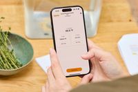 Person holding a smartphone displaying a cooking app interface for the Anova Culinary Precision Cooker 3.0 with temperature settings visible