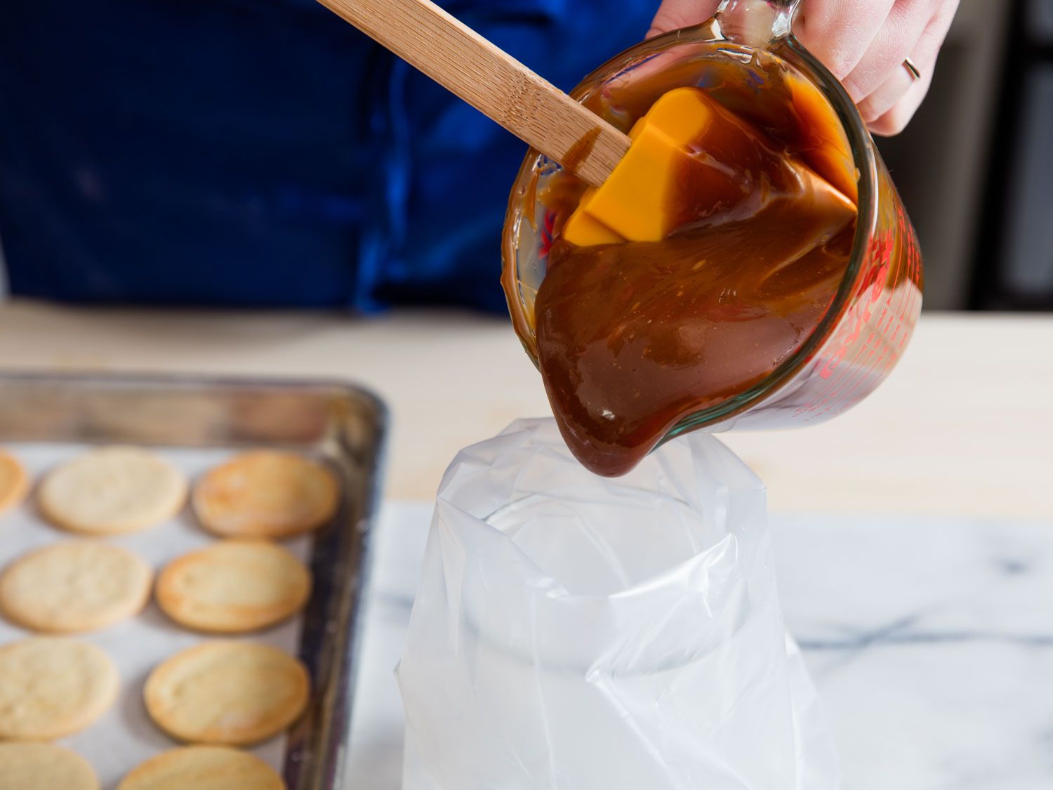 Author transferring cajeta from a liquid measuring cup to a pastry bag, scraping out the thick mixture with a spatula.