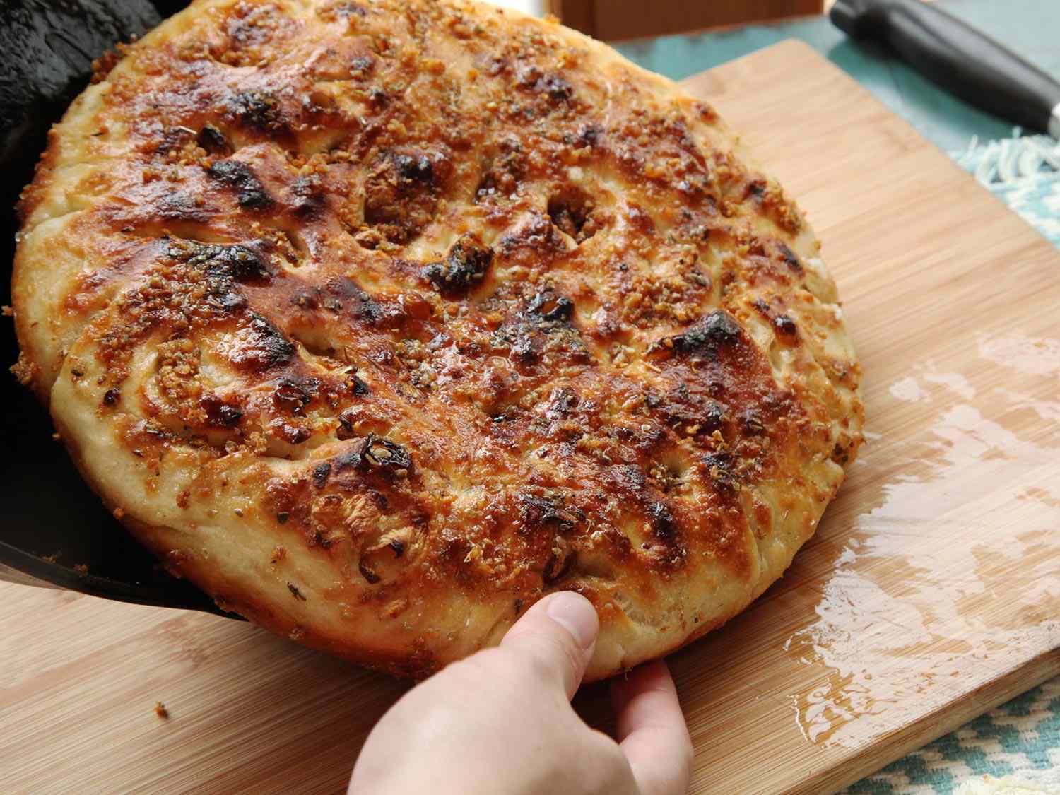 Sliding no-knead garlic focaccia out onto a cutting board from a cast iron skillet.