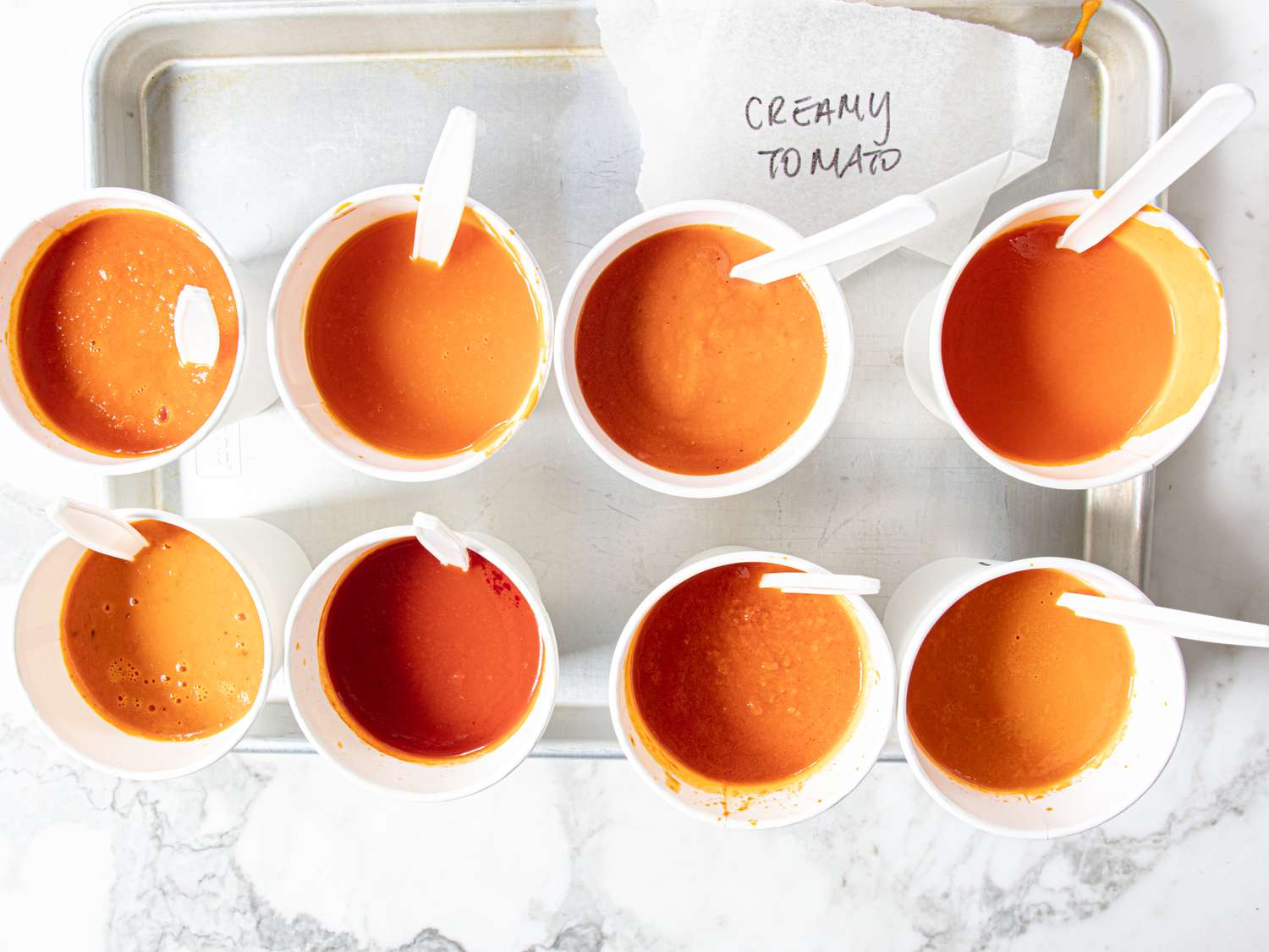 Various bowls of creamy tomato soup with spoons arranged on a tray for a taste test
