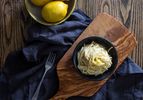A bowl of pasta al limone on an olive wood cutting board with a dark blue linen napkin.