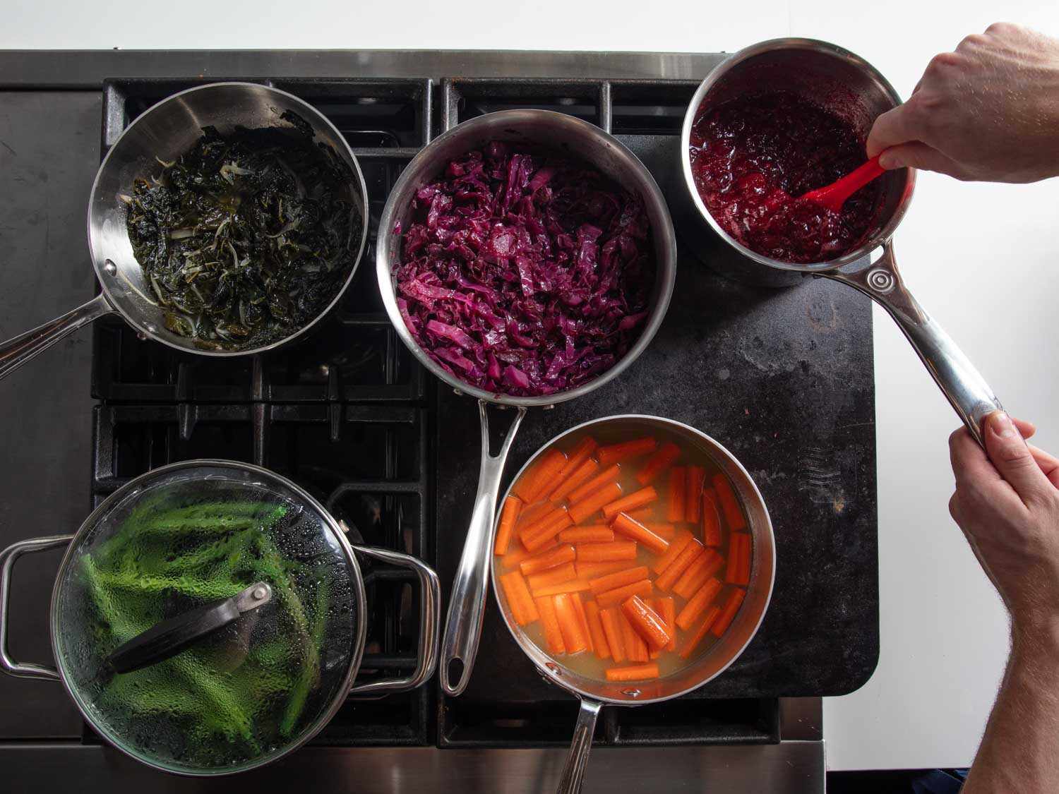 Overhead view of a Baking steel set up over two burners of a gas range, with various saucepans of vegetables cooking all at the same time.