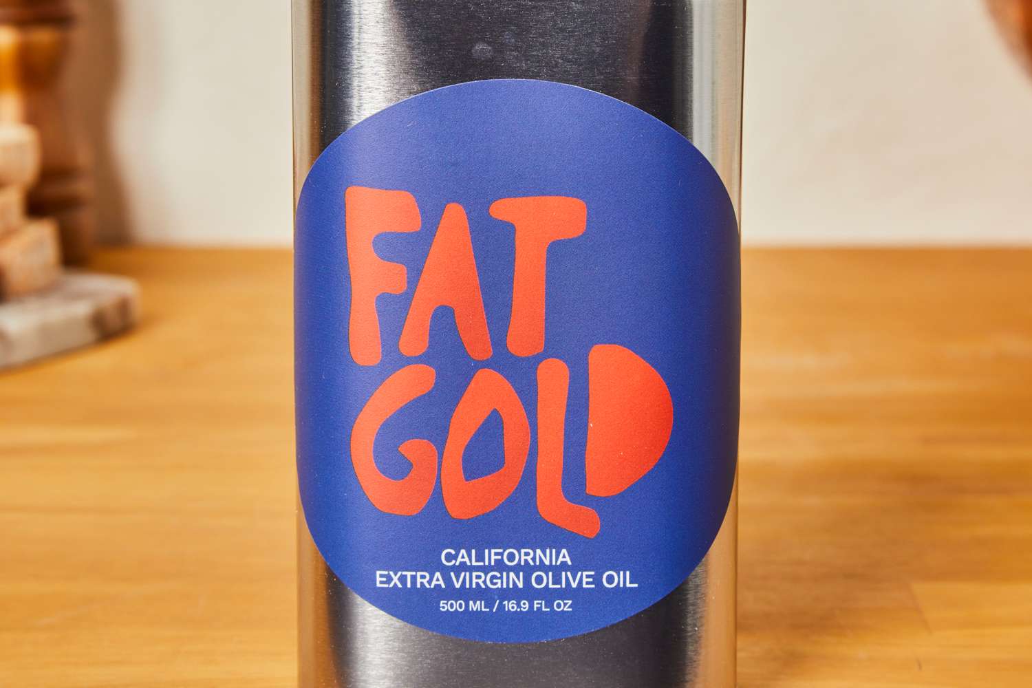 A metal bottle labeled Fat Gold California Extra Virgin Olive Oil on a wooden surface