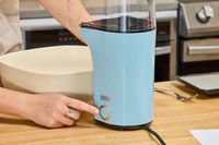 A person presses a button on the Dash Hot Air Popcorn Maker