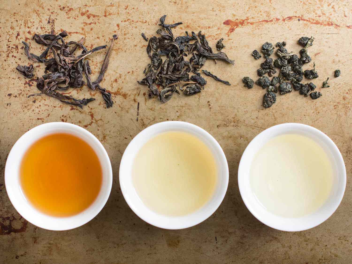 Three white cups of oolong tea next to their respective tea leaves