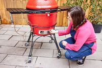 A person opens a vent on the bottom of the Kamado Joe Classic II Charcoal Grill