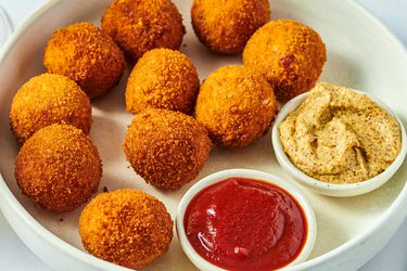 Plate of Ohio sauerkraut balls with one ball open, small bowls of ketchup and mustard.