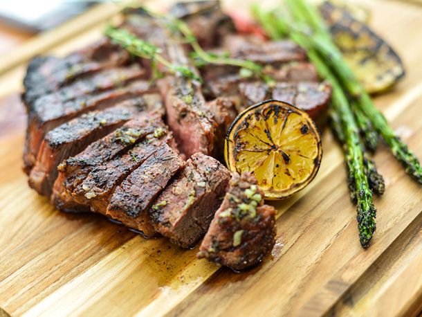Grilled porterhouse, sliced on a cutting board, drizzled with herb butter, served with a charred lemon half and grilled asparagus. 