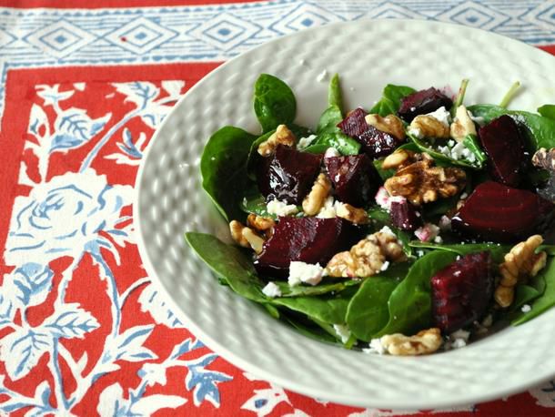 Closeup of spinach salad with beets and walnuts, served in a bumpy-rimmed bowl.