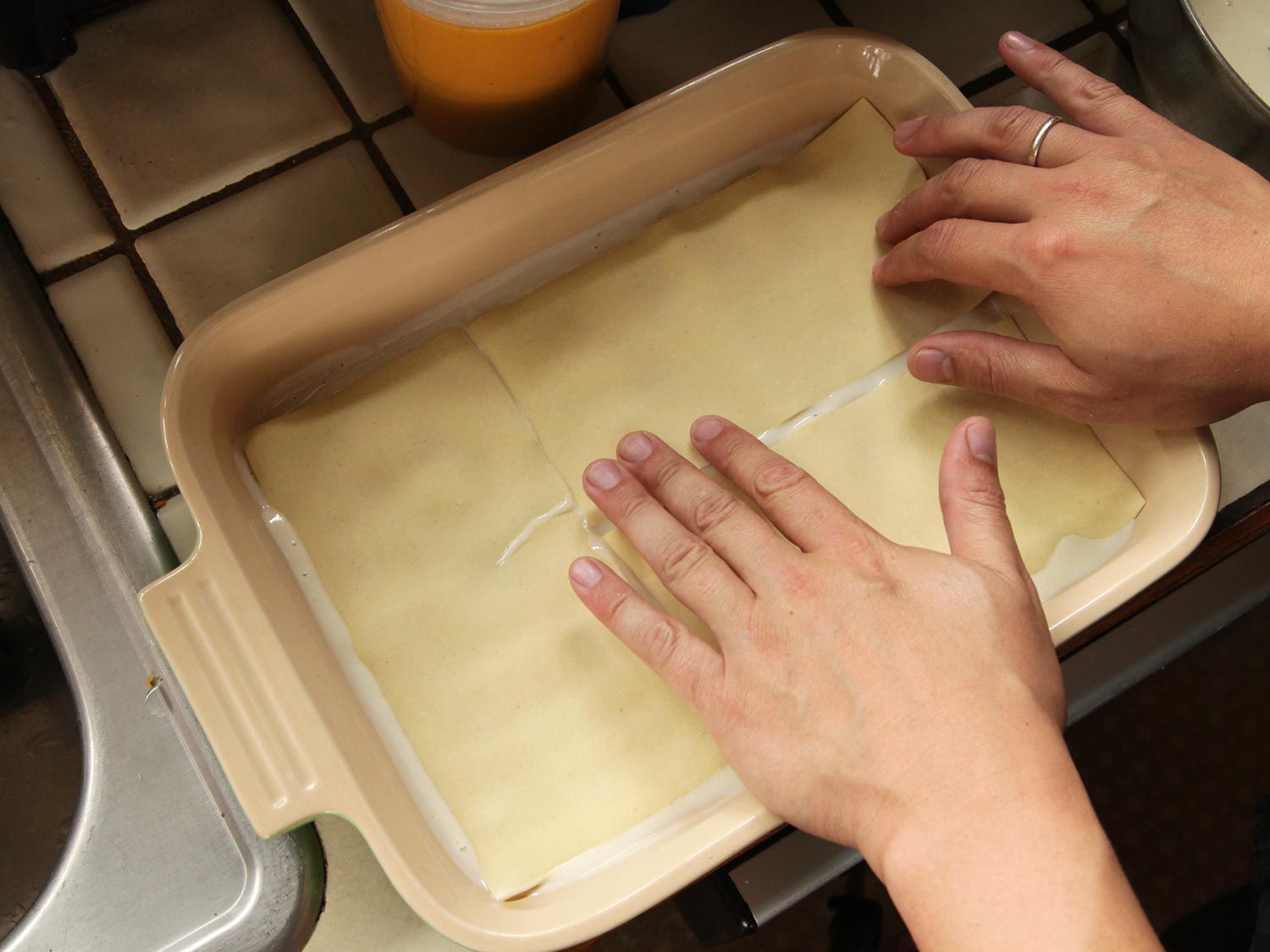 Layering pasta sheets over white sauce in a baking dish.
