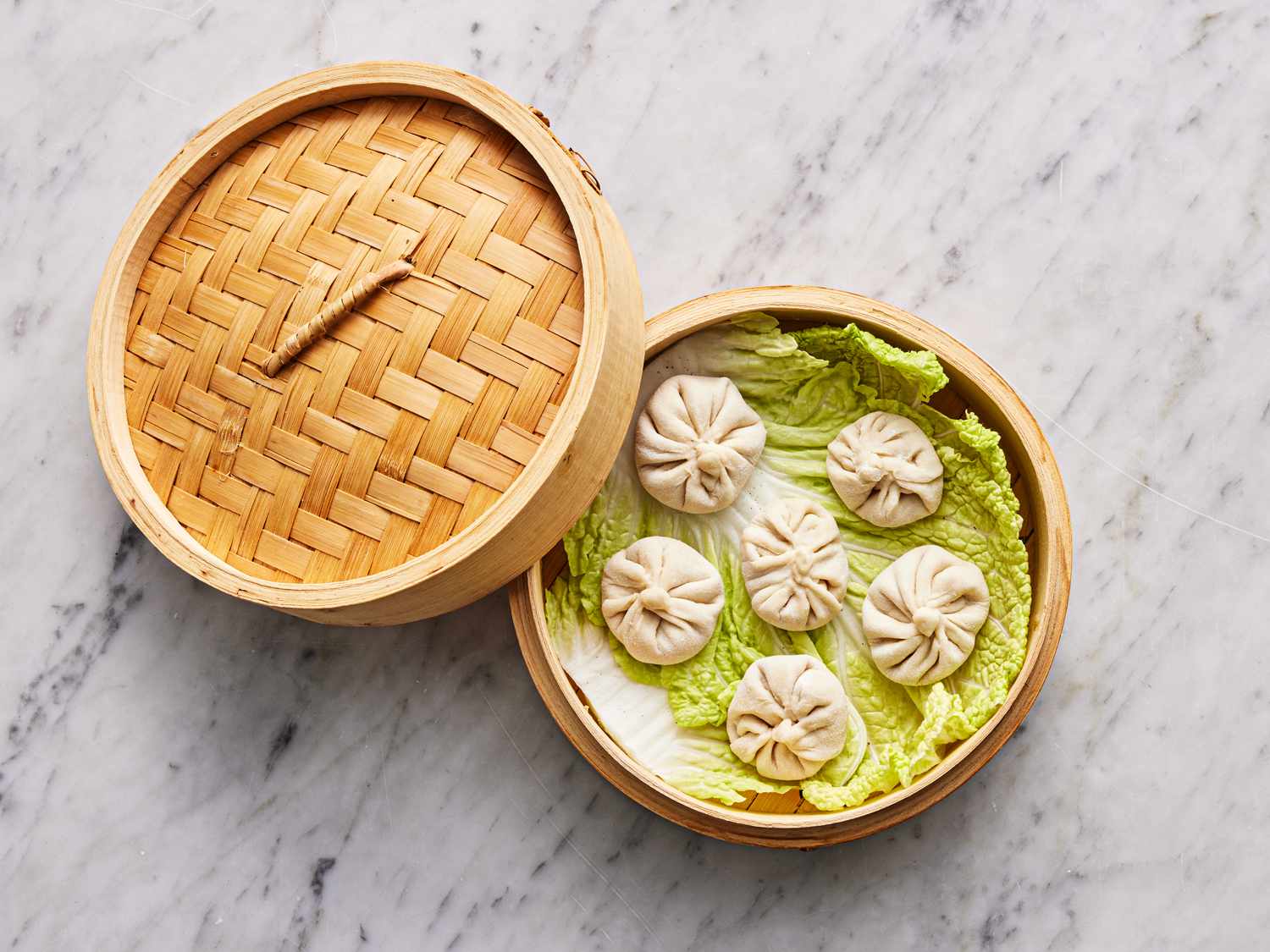 Overhead view of dumplings in a bamboo steamer lined with lettuce
