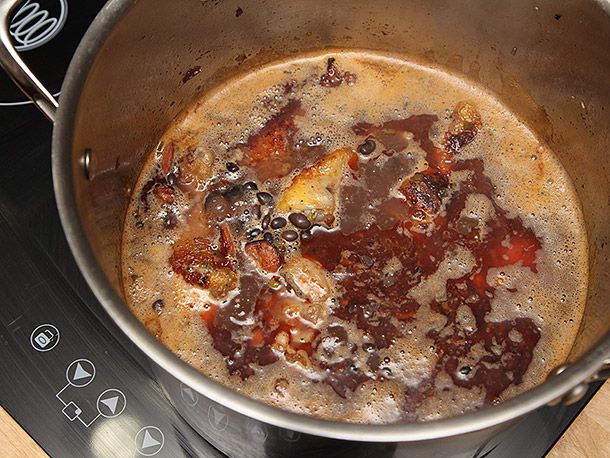 Adding cooking liquid and dried black beans to a stock pot and bringing it to a simmer to cook for black bean soup.