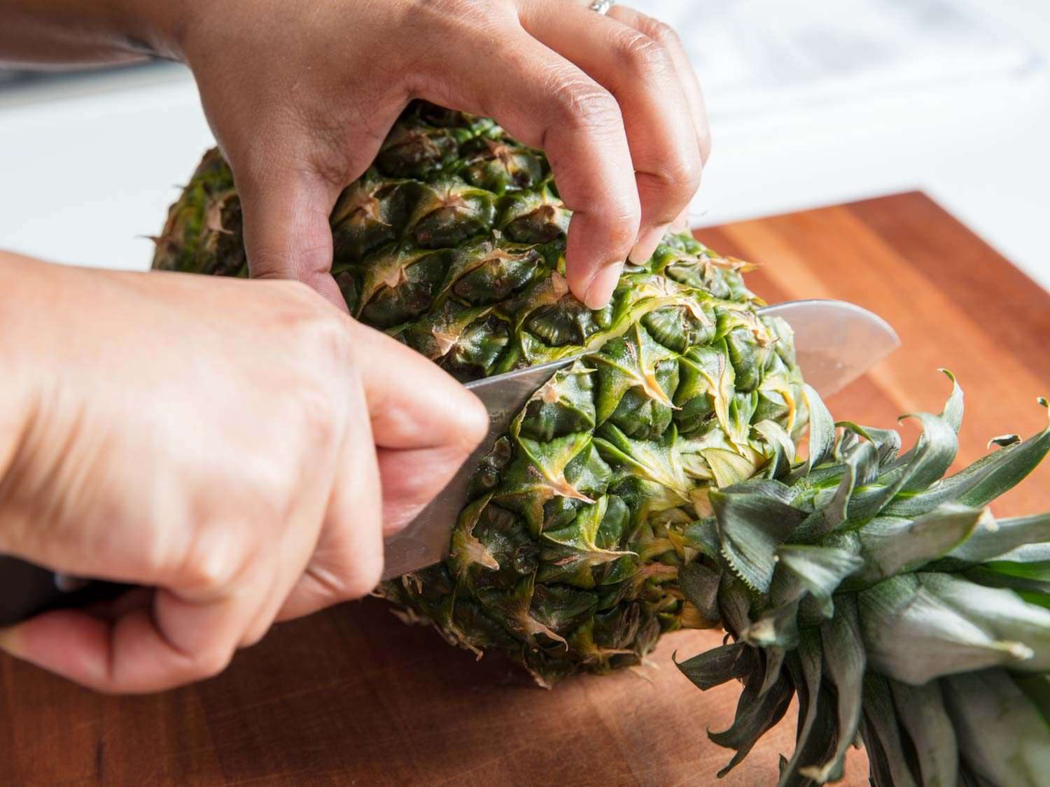 A knife slicing off the top of a pineapple.