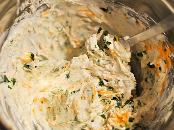 Mixing cheddar cheese and cilantro into cream cheese in a bowl.