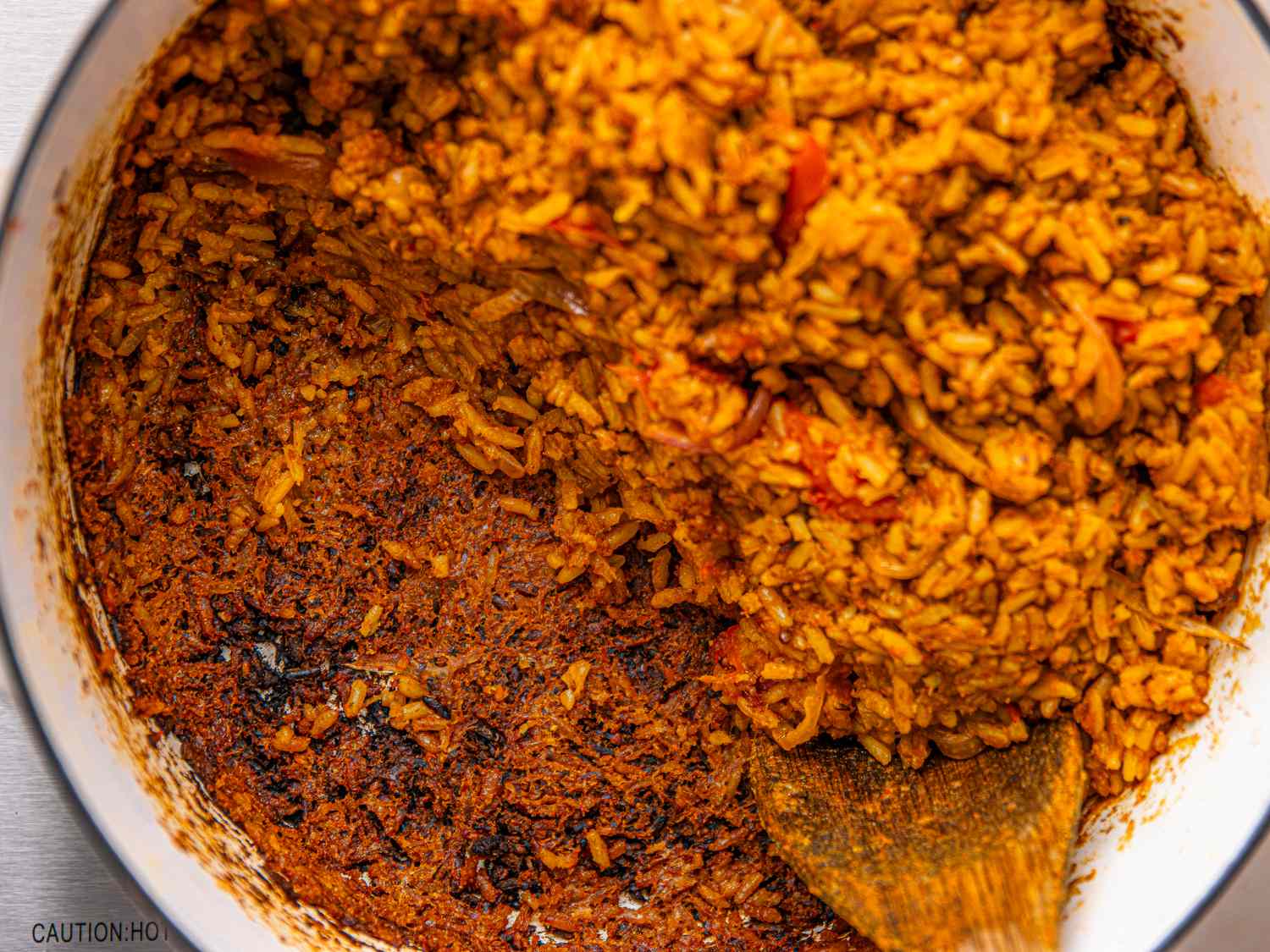 A pot of Nigerian jollof rice with a wooden spoon