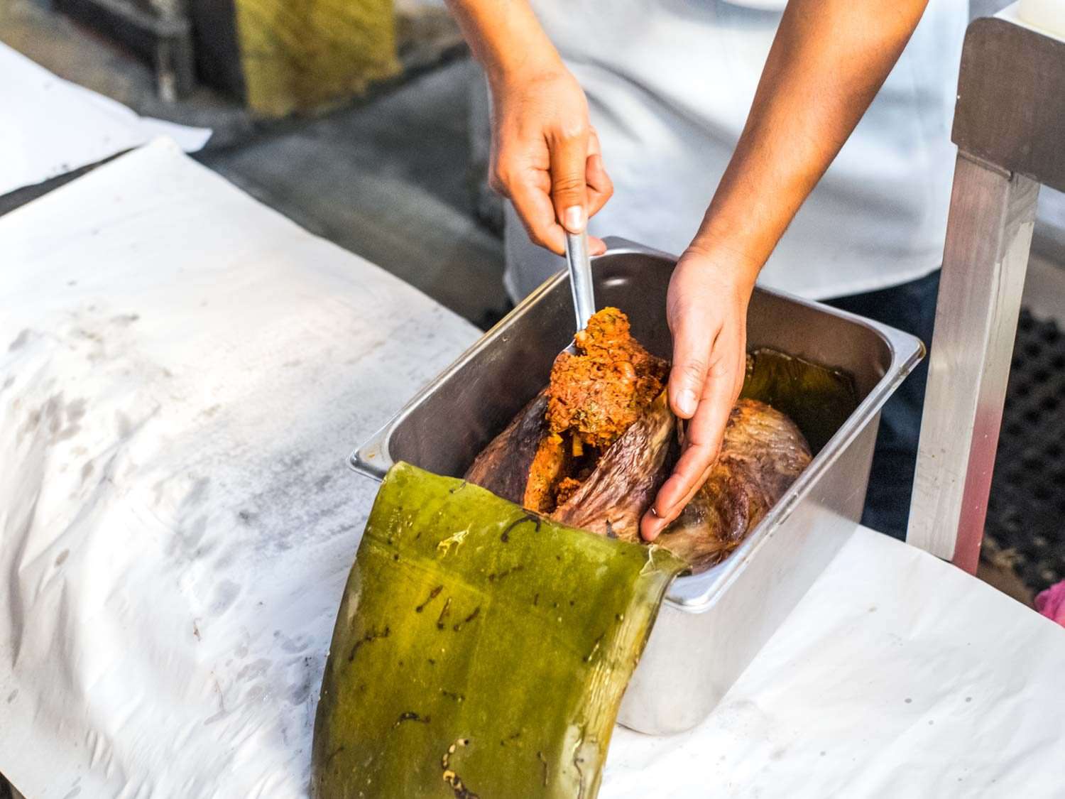 Serving barbacoa from a metal pan lined with a maguey leaf.