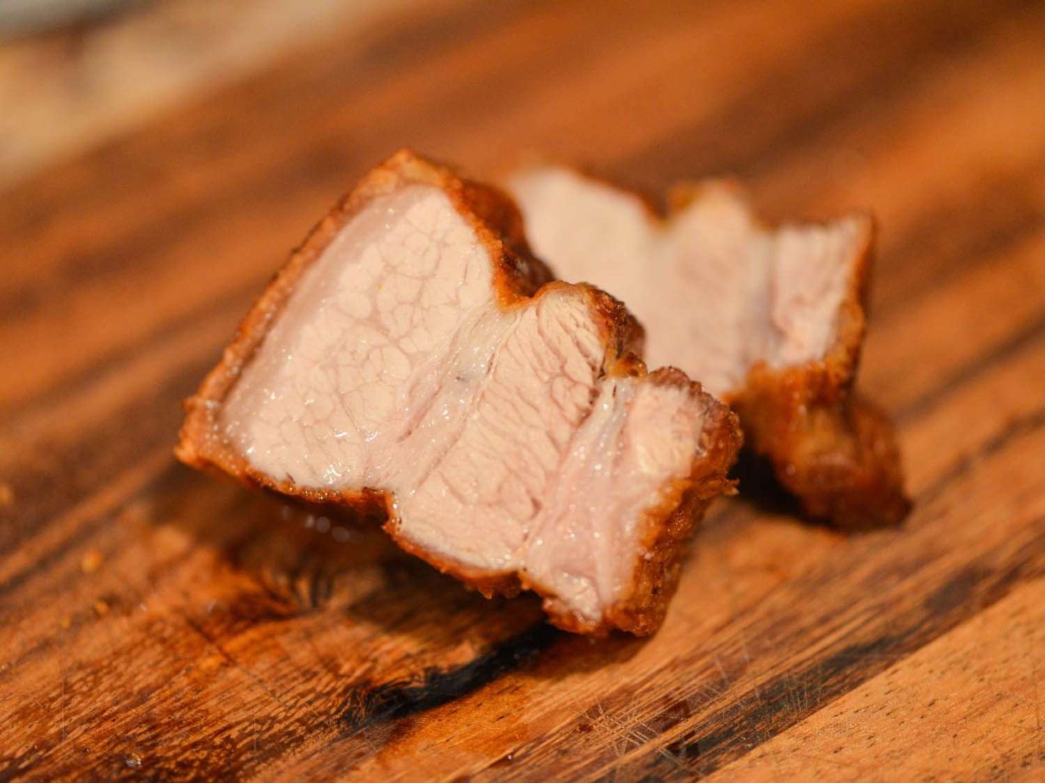 Two small cuts of cooked lechon kawali resting on a wooden surface.