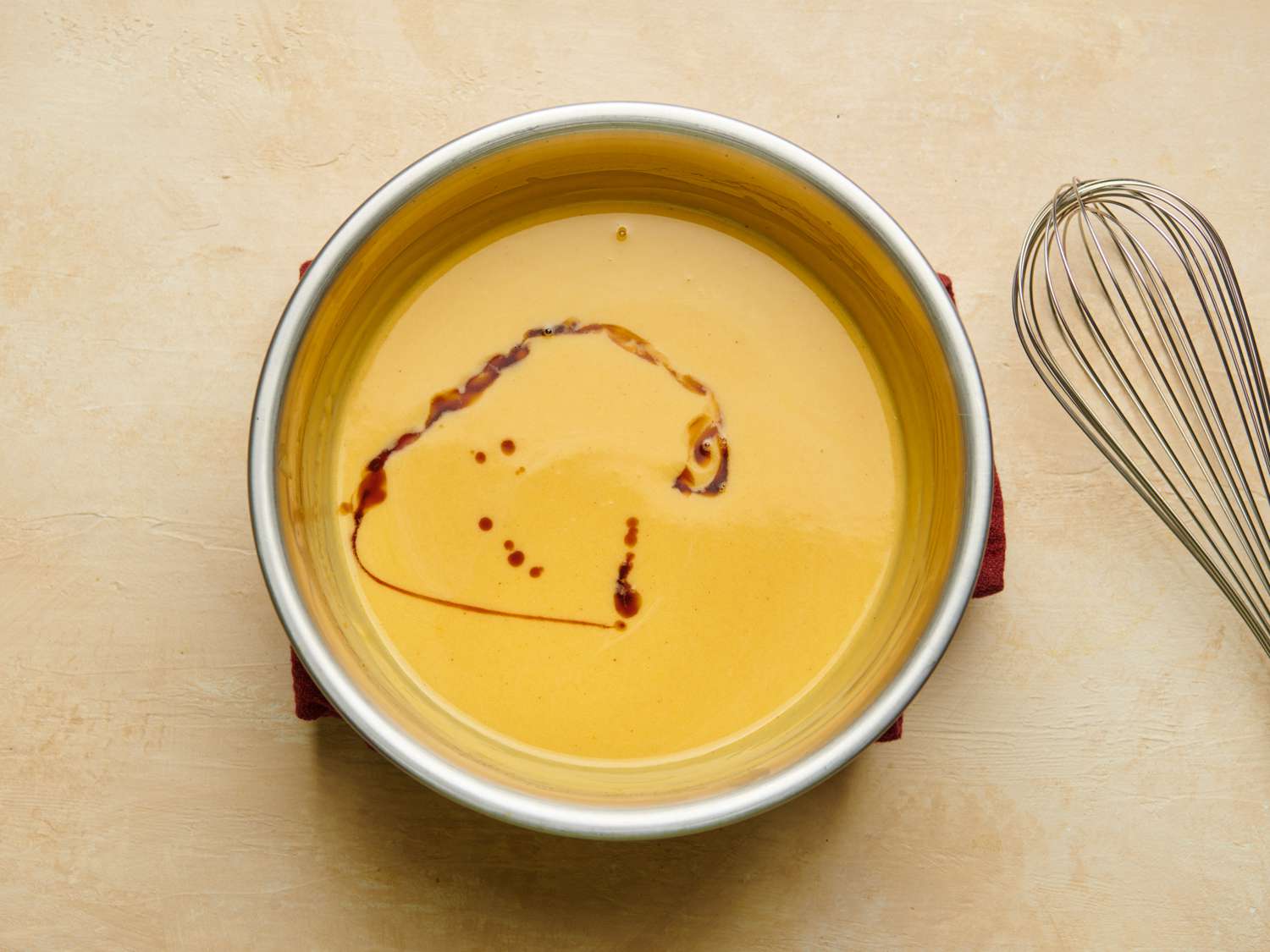 The cooked advocaat, in a metal bowl, with vanilla extract drizzled over the top. A whisk is alongside.