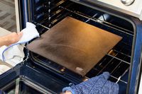A person placing a pizza steel into the oven.