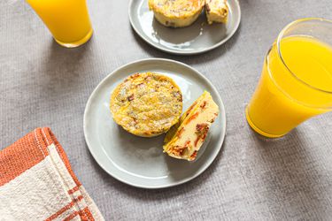 Two plates with muffin tin bacon egg bites next to glasses of orange juice