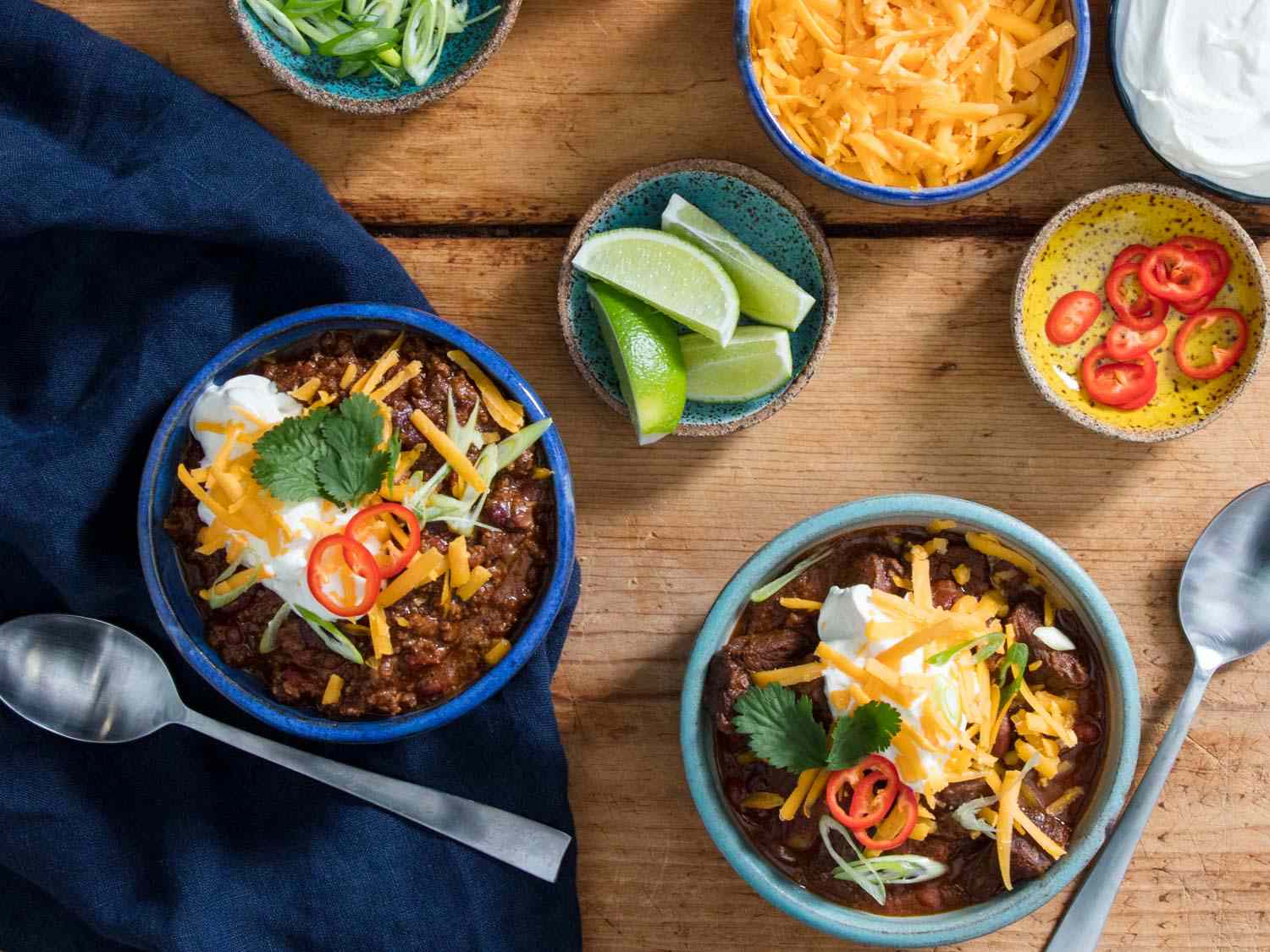 Two bowls of pressure cooker chili topped with cheese, sour cream, cilantro, chile slices, and lime wedges.