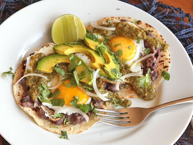 Huevos Rancheros Verdes, or Fried Eggs With Green Salsa and Refried Beans, on a plate with a fork and lime wedge.
