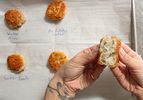 Hands holding a halved fried potato patty with several patties on a marked baking sheet in the background