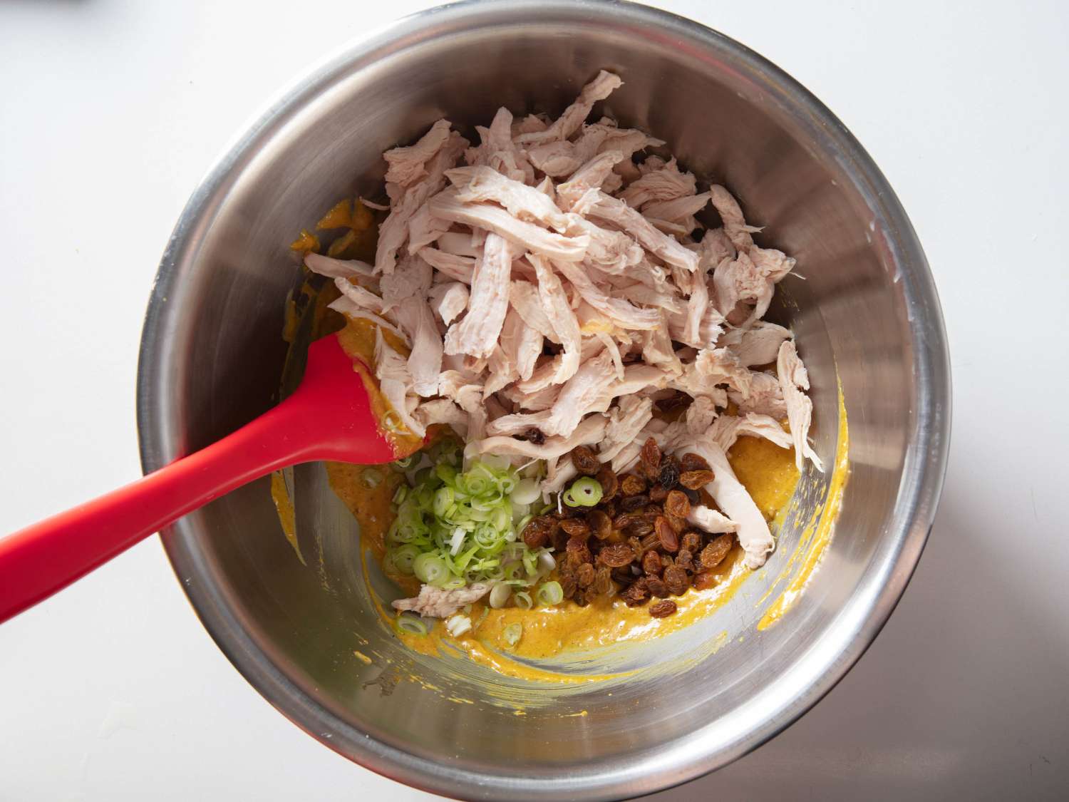 Mixing together all of the ingredients for curry chicken salad in a mixing bowl.