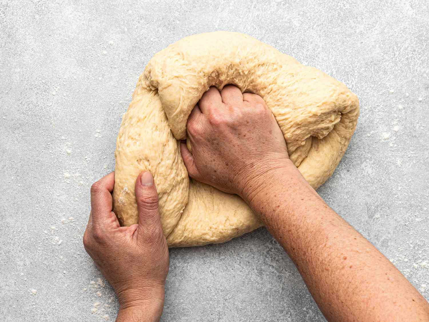 Kneading empanada dough with hands, pressing and folding on a floured surface.