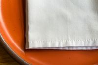 A close-up of a white napkin on the edge of an orange plate