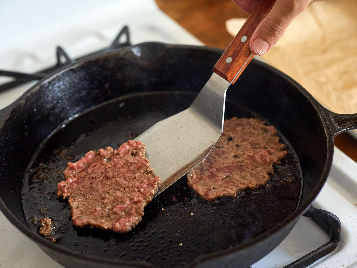 an offset metal turner lifting a smash burger from a cast iron skillet. 