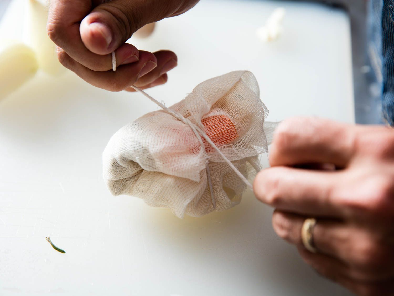 A sachet of aromatic herbs and vegetables being tied up by a pair of hands.