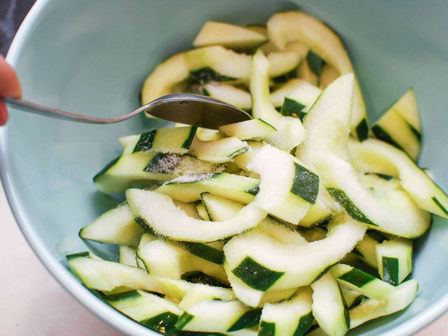 Cucumber slices tossed in salt in a mixing bowl. 