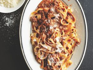 Lamb bolognese tossed with fettucine noodles and sprinkled with freshly grated cheese on a white oval platter. 