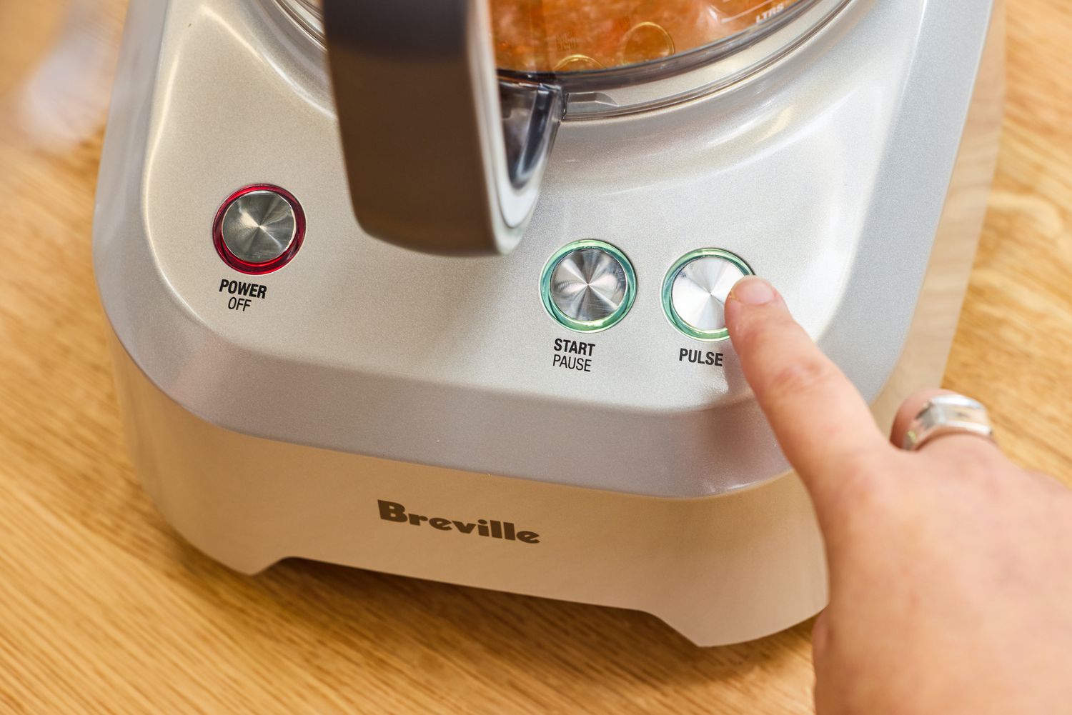 A person presses the 'PULSE' button on the Breville BFP660SIL Sous Chef 12-Cup Food Processor