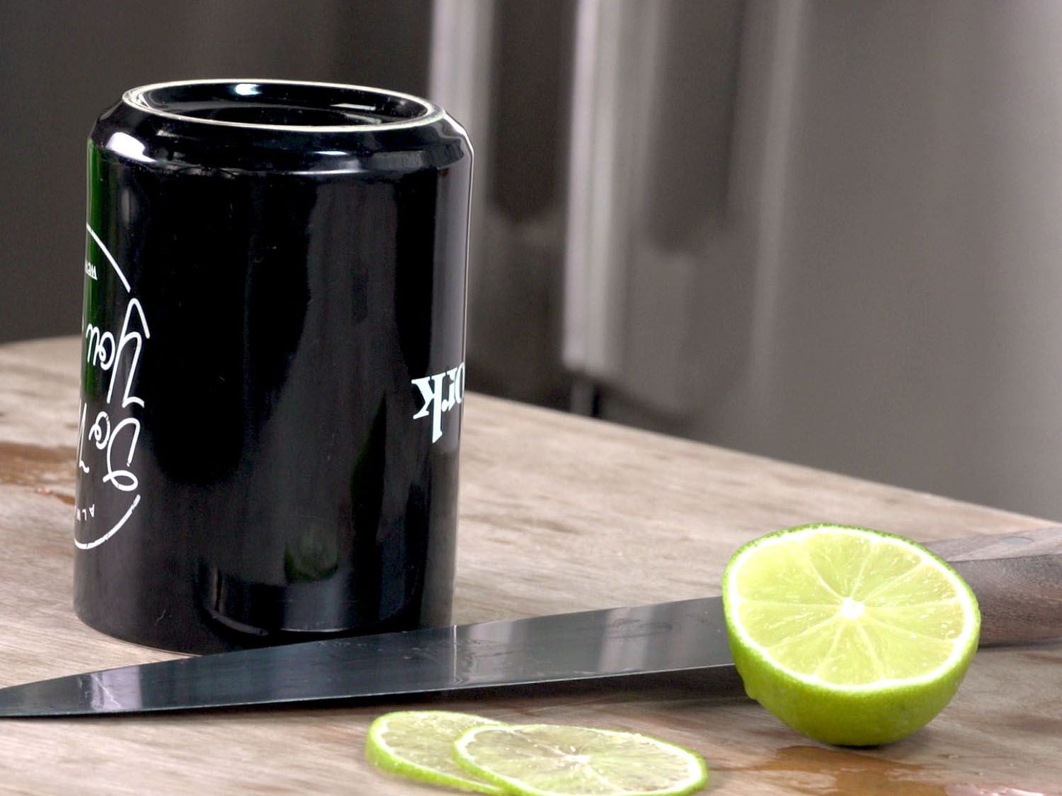 An upended coffee mug is set on a cutting board next to a chef's knife and a thinly sliced lime.