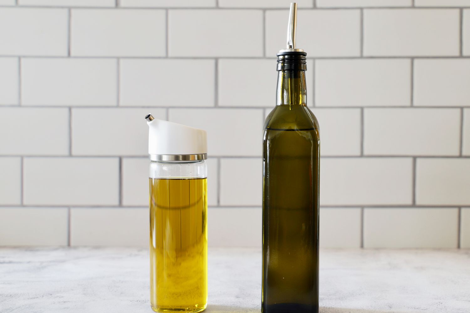 OXO Precision Pour Glass Dispenser - 12 oz. and Zulay 17-Ounce Olive Oil Dispenser Bottle on a marble counter