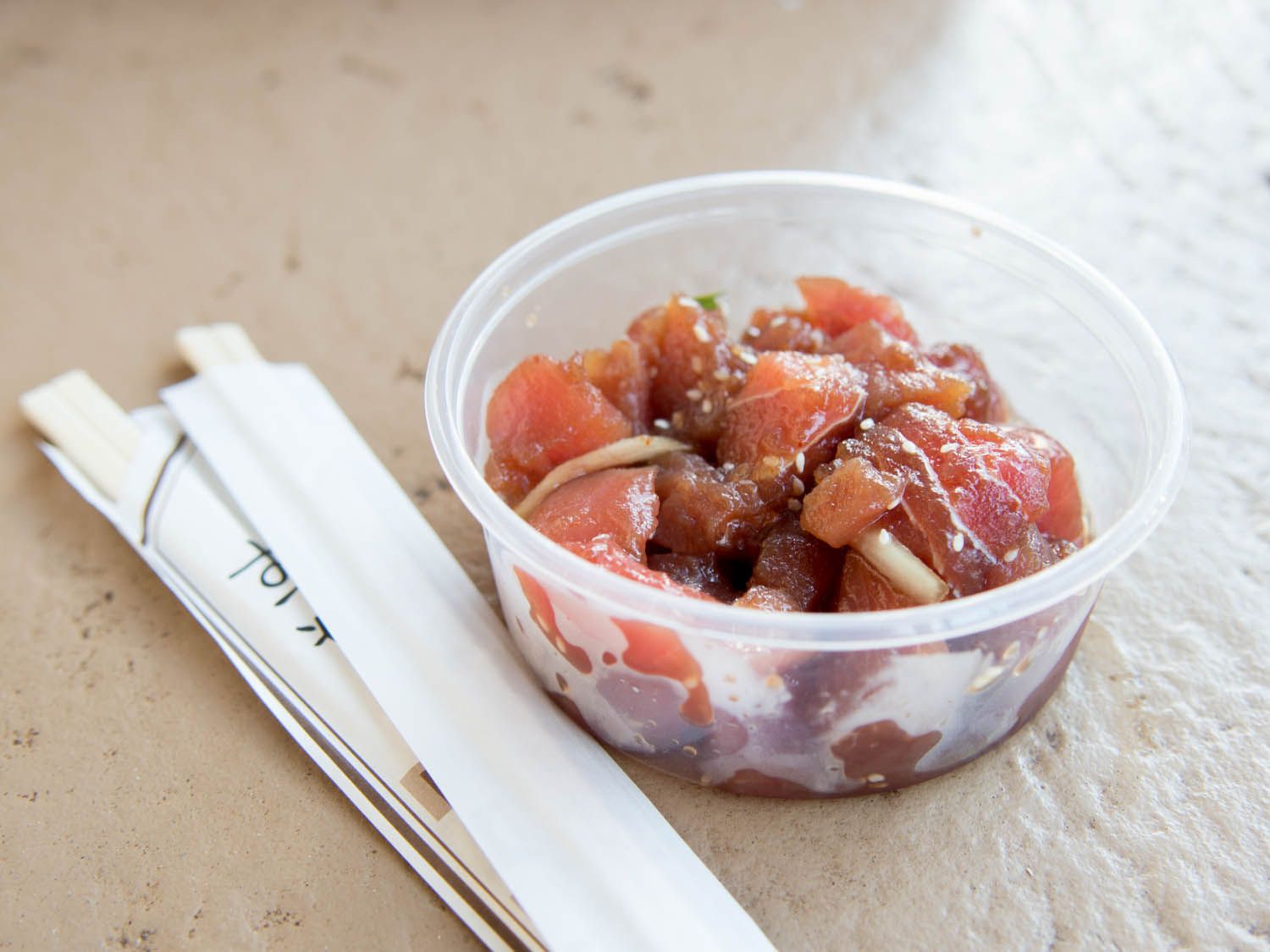 A take out container of ahi poke, flanked by two pairs of disposable chopsticks.