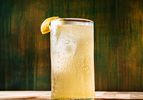 A glass filled with a fizzy lightcolored beverage garnished with a lemon wedge placed on a wooden surface