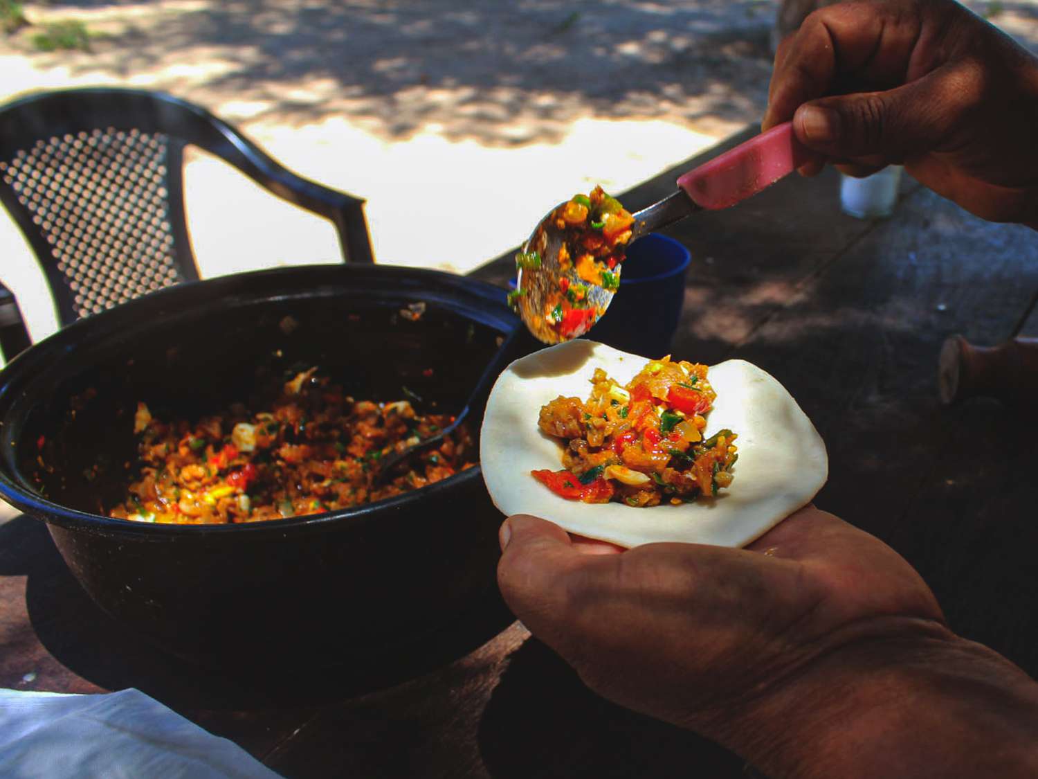 Homemade empanada shells being fillied with pan-fried goat
