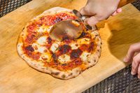 A person cuts a pizza made in the Gozney ARC XL Compact Pizza Oven