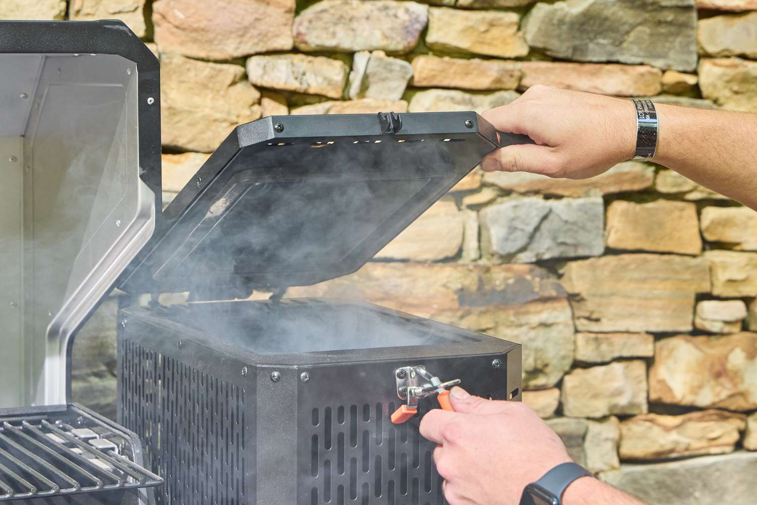 A person opens the smoker box on the Masterbuilt Gravity Series 1150 Digital Charcoal Grill and Smoker