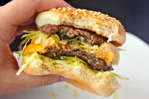 A better Big Mac is held up for the camera. Several bites have been taken from the sandwich.